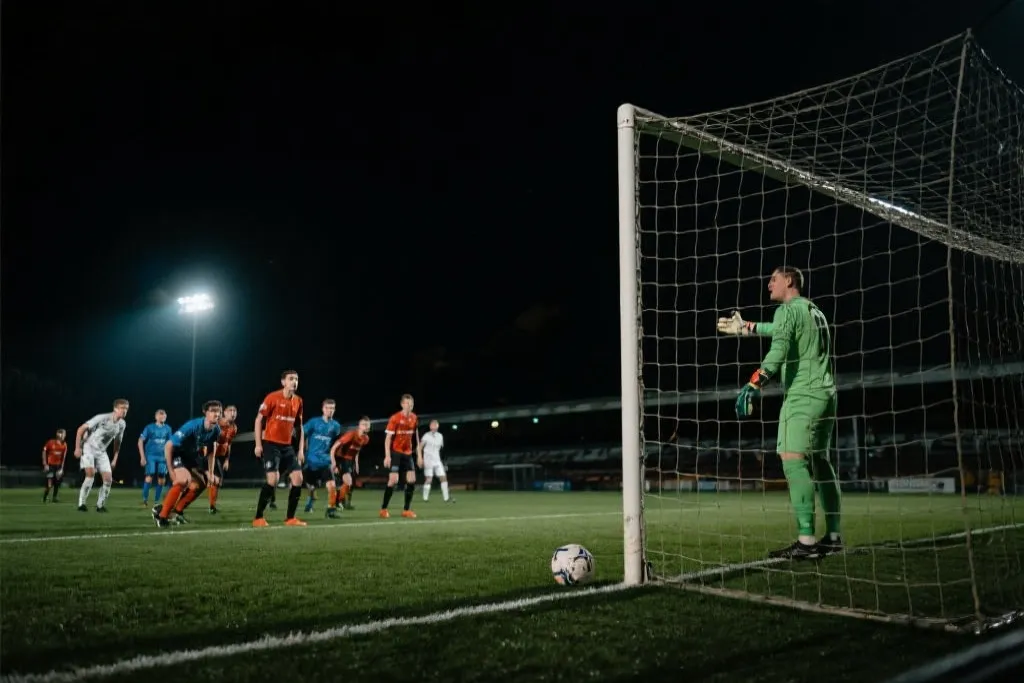 夜晚球场补时角球时门将指挥防线并专注观察来球，电影感体育纪实